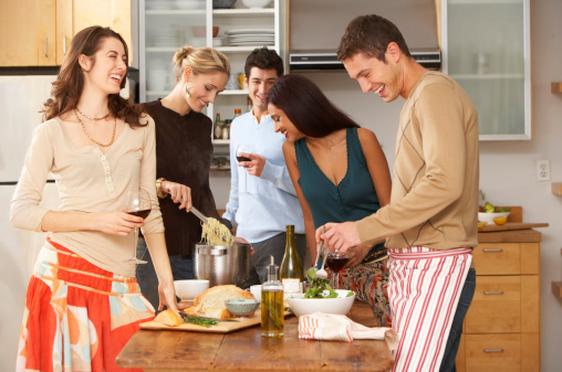 Group of young people in kitchen, couple preparing food, laughing